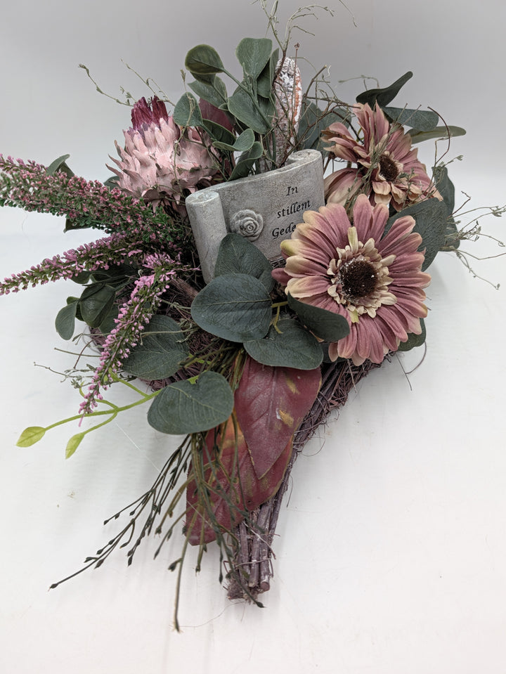 Trauergesteck in Rosa mit Gerbera, Protea, Heidezweigen und Eukalyptus auf hellem Geflecht, Breite 30 cm