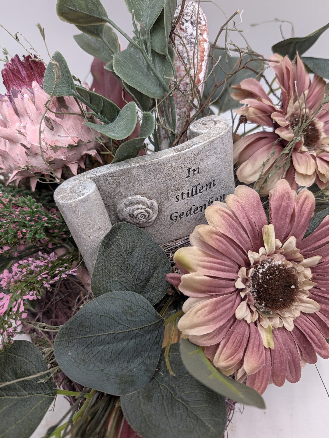 Nahaufnahme der Tafel in Steinoptik mit Rosenrelief und Schriftzug In stillem Gedenken zwischen rosa Gerbera