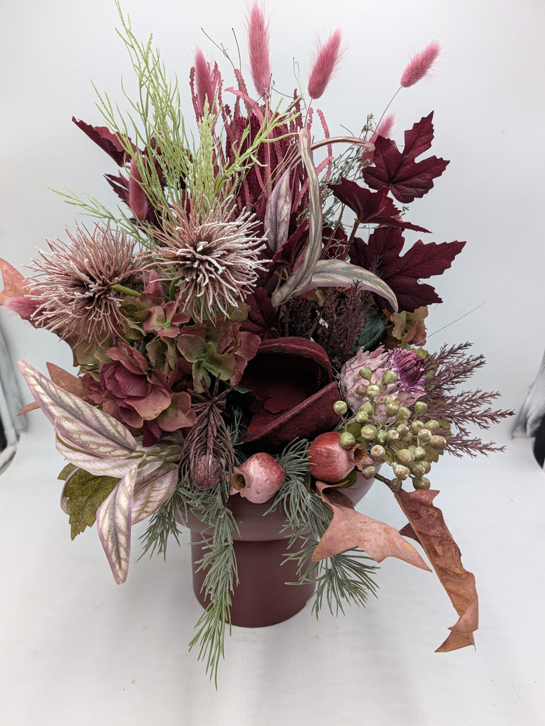 Hohes Kunstblumengesteck mit weinroten Blättern, grünen Beeren, Mohnkapseln und Nadelzweigen in dunkelroter Vase