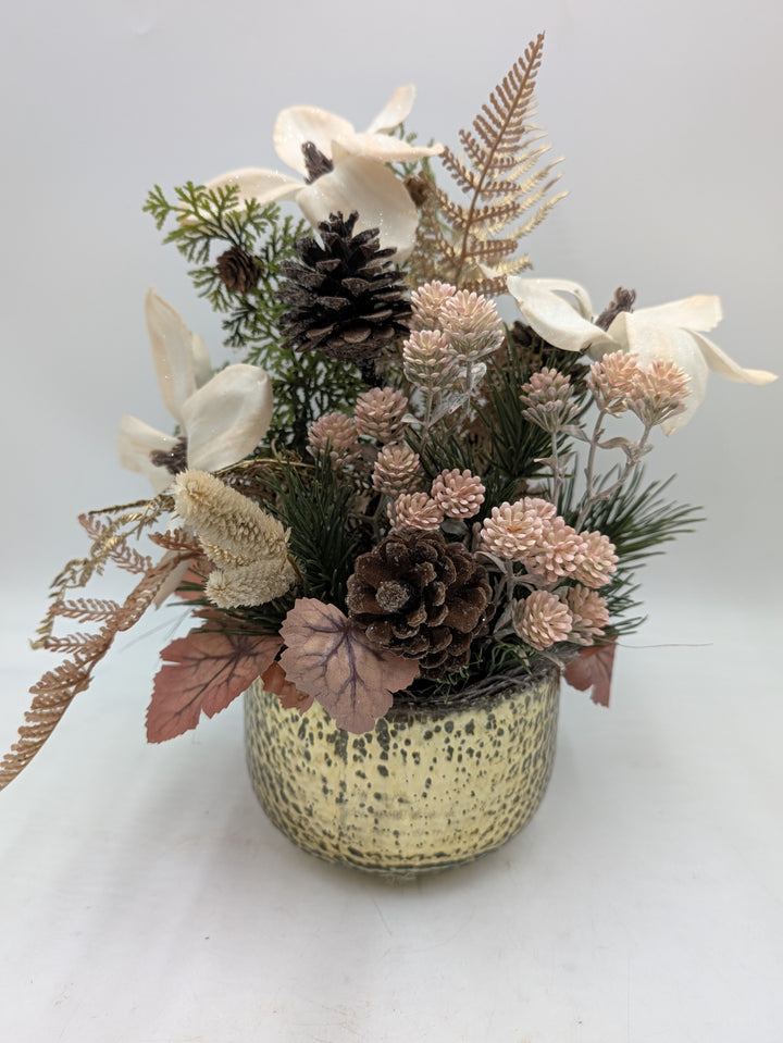 Wintergesteck mit cremefarbenen Magnolien, braunen Zapfen und rosa Dolden in gesprenkeltem cremefarbenem Topf