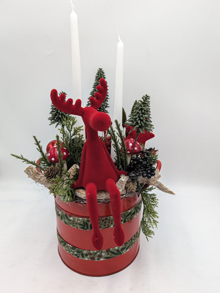 Weihnachtsgesteck in roter Dose mit rotem Elch, zwei weißen Stabkerzen, Tannenbäumchen und Fliegenpilzen