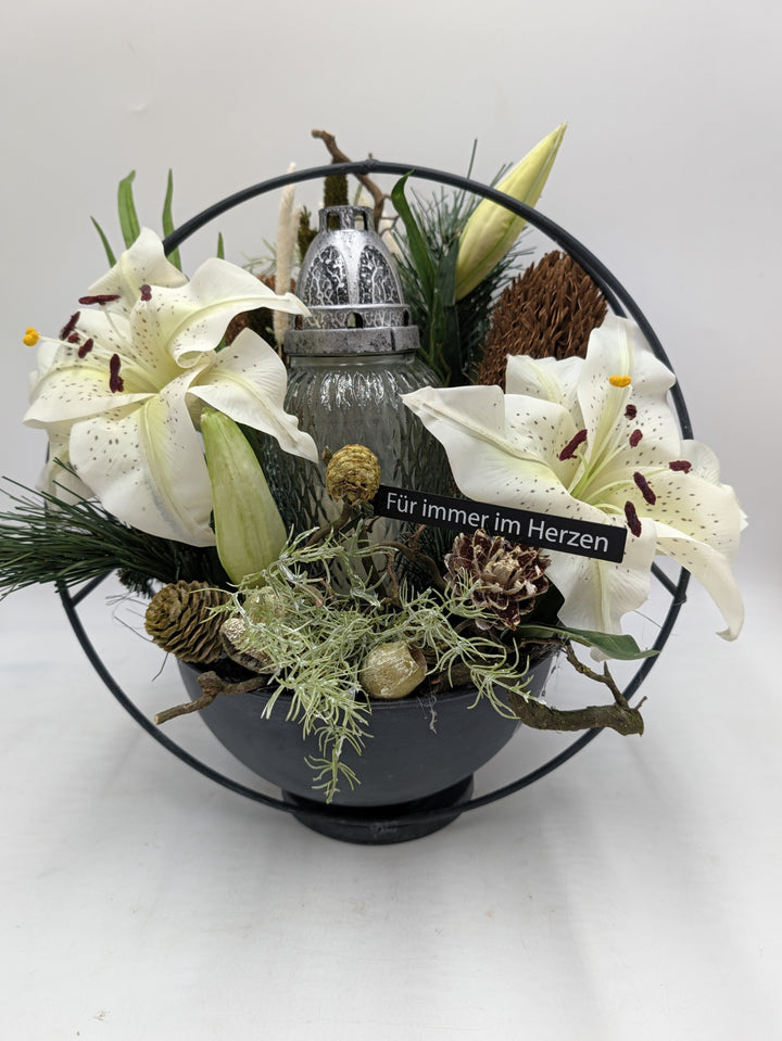 Grabgesteck mit weißen Lilien, Grablicht und Zapfen in schwarzer Schale mit Metallring, Schild Für immer im Herzen