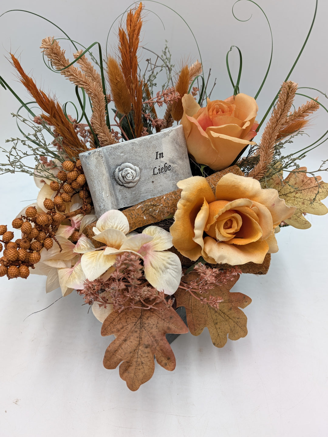 Trauergesteck von vorn: Tafel In Liebe mit Rose, orange Rosen, Beerenzweige und Eichenblätter in grauem Gefäß