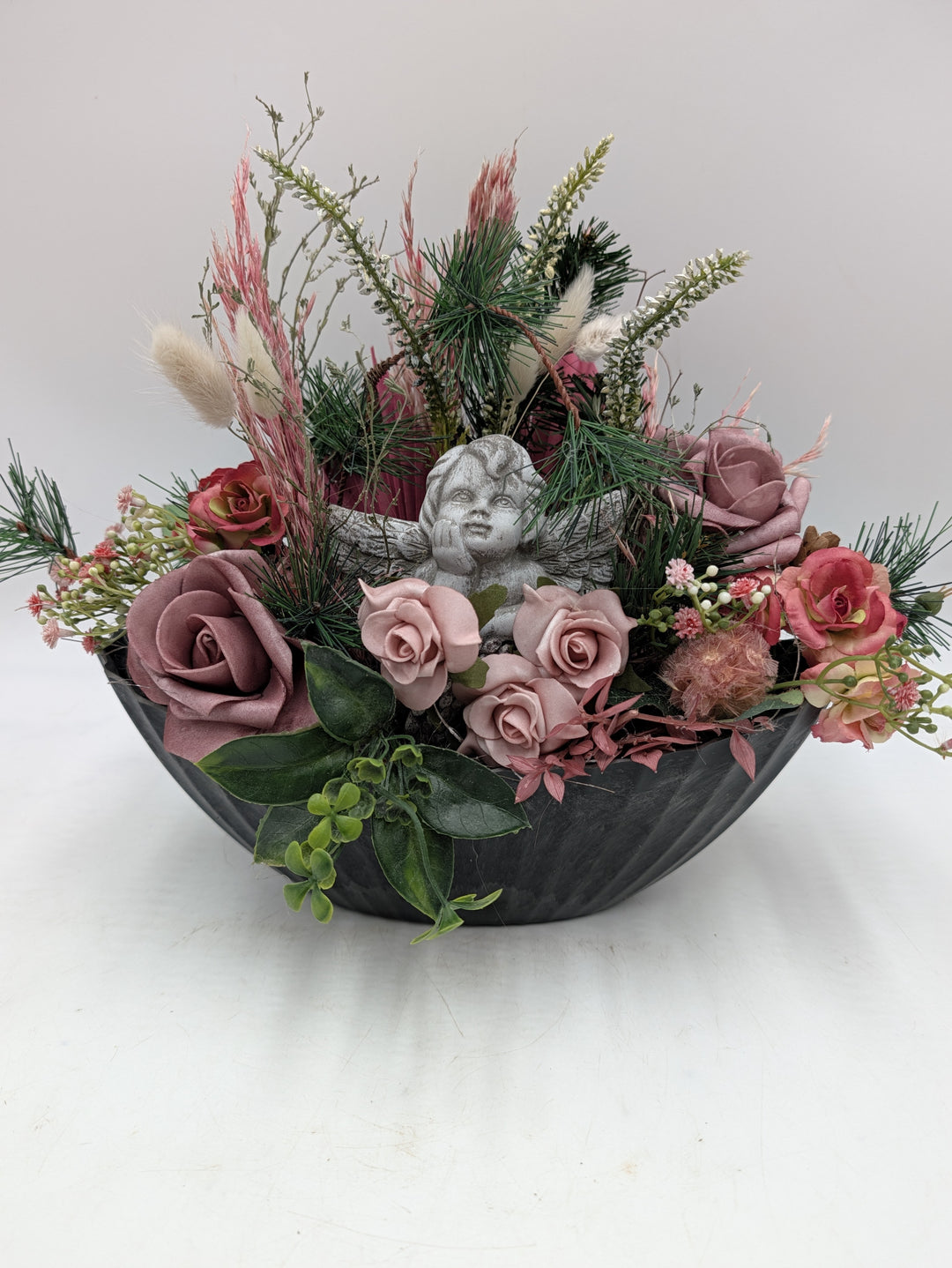Trauergesteck in grauer Schale mit grauem Engel, altrosa Rosen, Kiefernzweigen und rosa Gräsern