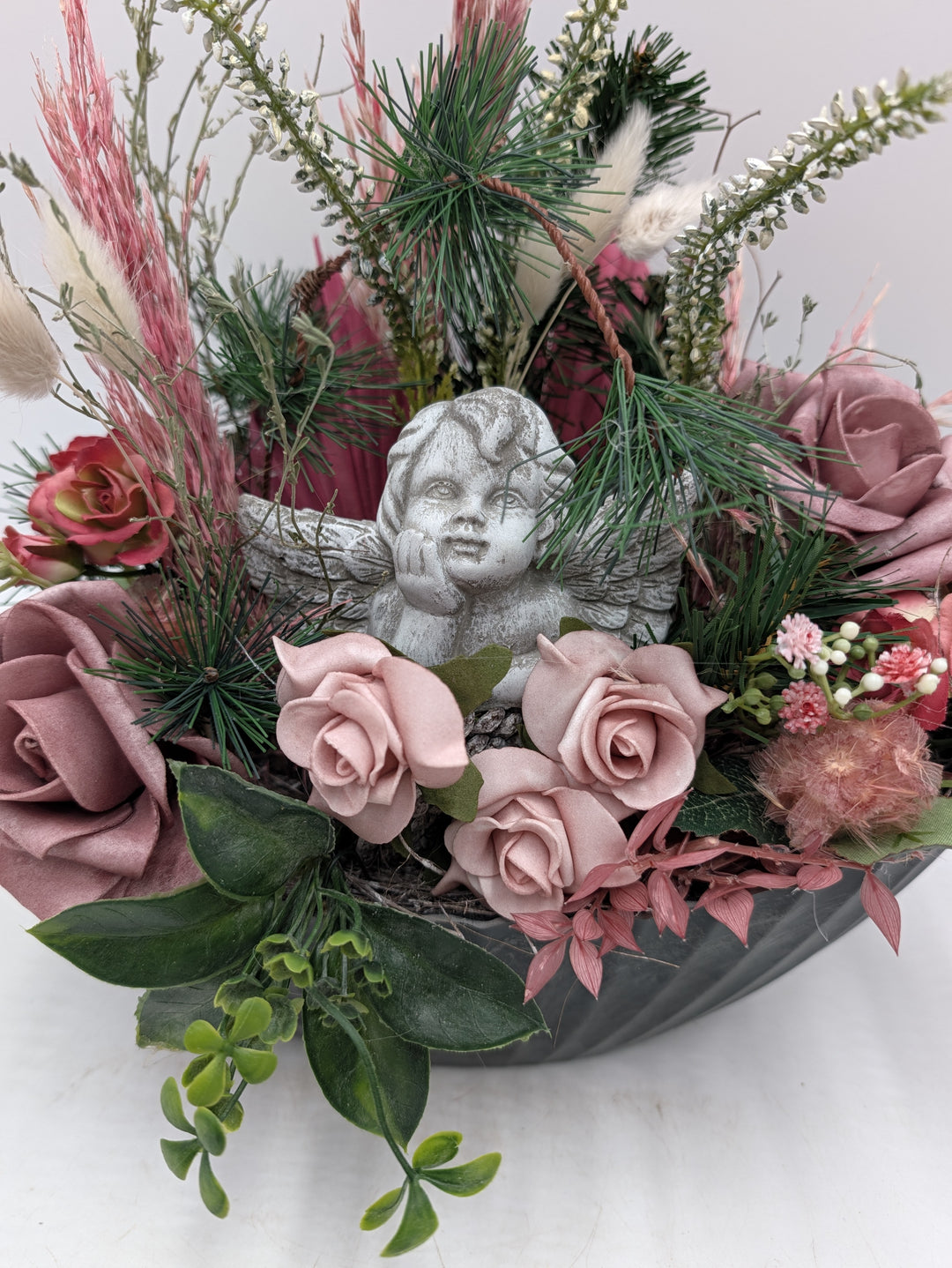 Nahaufnahme des Engels zwischen puderrosa Rosen, grünen Blättern, Heideblüten und Kiefernnadeln