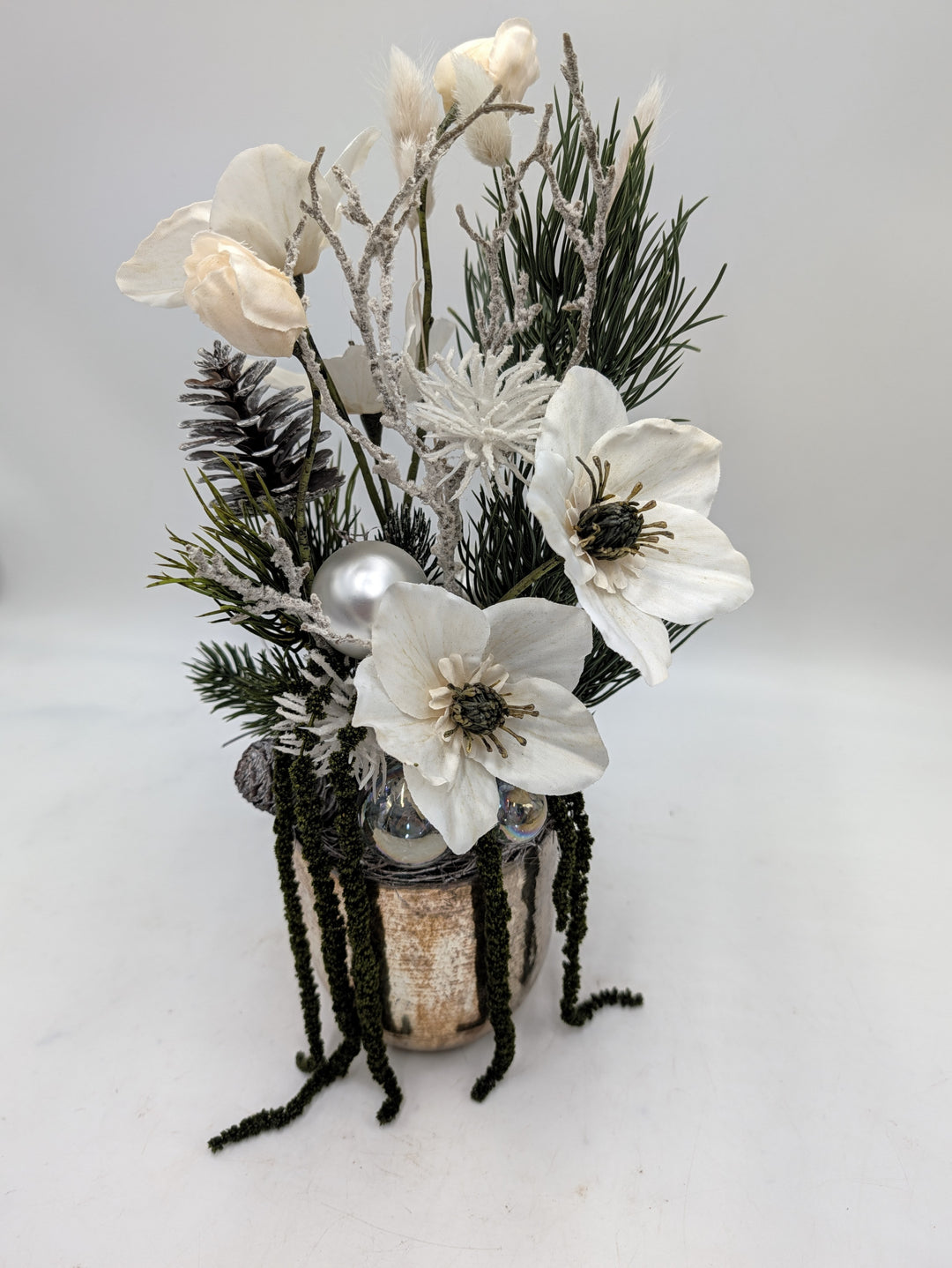 Seitliche Ansicht des Wintergestecks mit zwei weißen Christrosen, beschneiten Zweigen und hängenden grünen Rispen