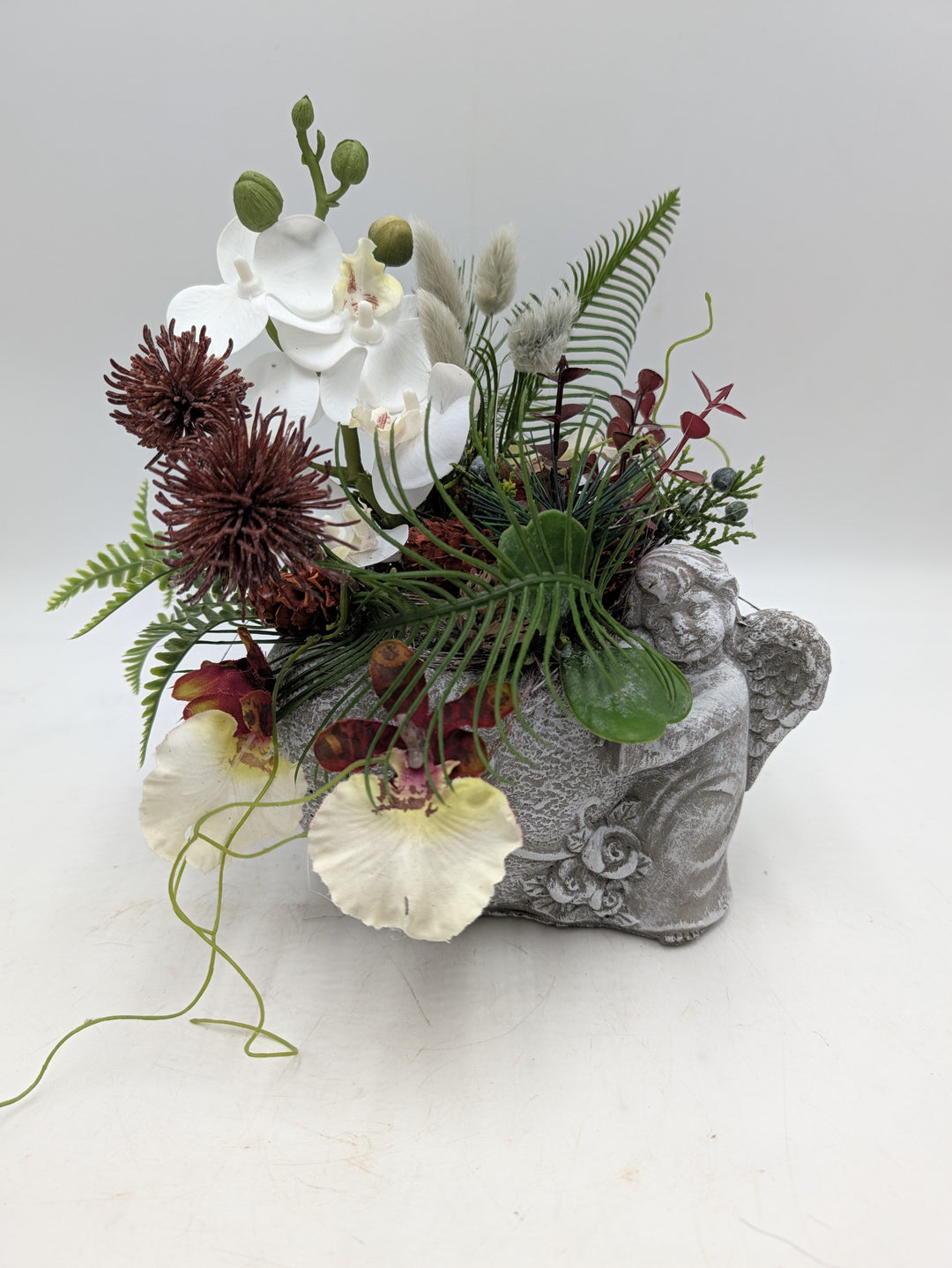 Trauergesteck mit weißen Orchideen, bordeauxfarbenen Chrysanthemen und Farn in grauem Engel-Gefäß
