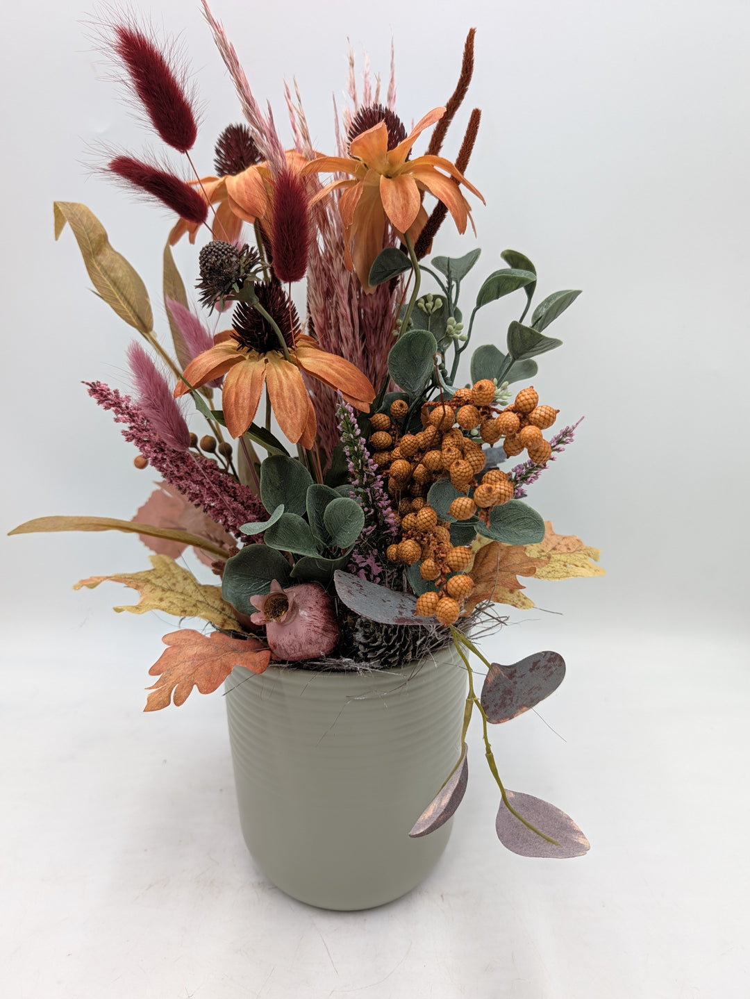Herbstgesteck mit orangefarbenem Sonnenhut, Beerendolde, Gräsern und Eukalyptus in grüngrauem Keramiktopf