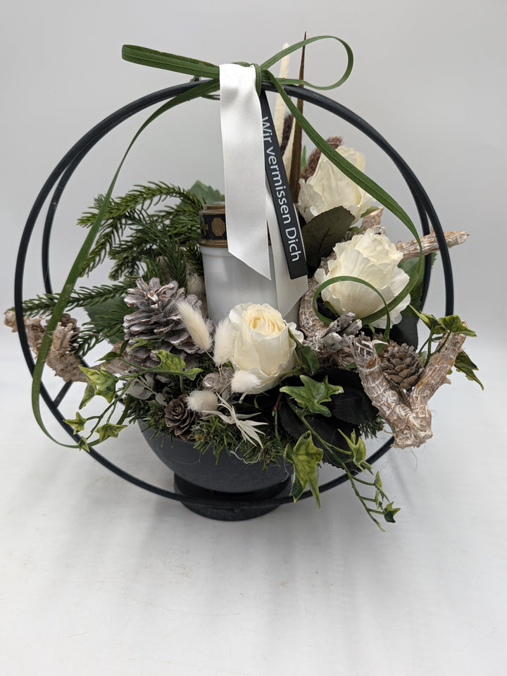 Trauergesteck im schwarzen Metallring mit weißem Grablicht, cremeweißen Rosen, Zapfen und Efeu