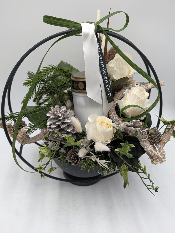 Nahsicht auf Grablicht mit goldenem Deckel, weiße Rosen, heller Zapfen, Tannenzweige und Satinband