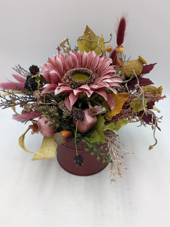 Herbstgesteck von vorn: altrosa Sonnenblume, gelbe Blätter, Zierkürbis und Gräser in dunkelrotem Topf