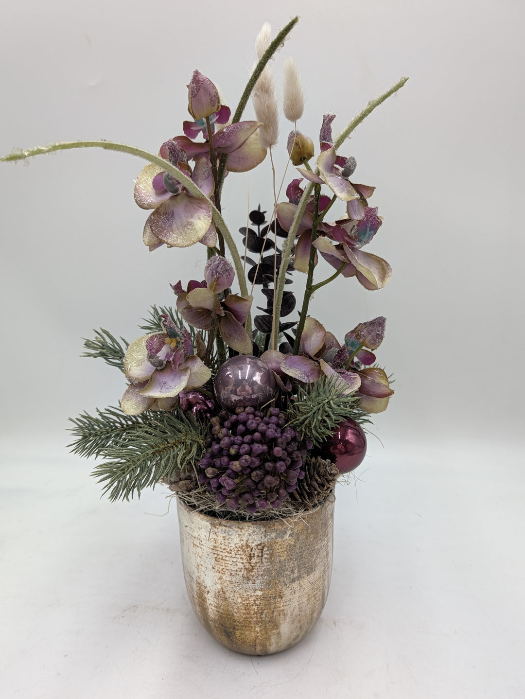 Weihnachtsgesteck mit lila-cremefarbenen Orchideen, Beeren, Kugeln und Tannenzweigen in goldenem Topf