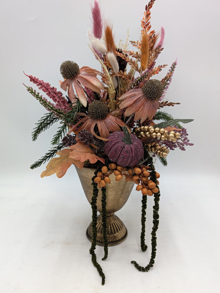 Herbstgesteck mit lachsfarbenem Sonnenhut, lila Kürbis und Gräsern in goldfarbener Pokalvase, hängender Amaranth