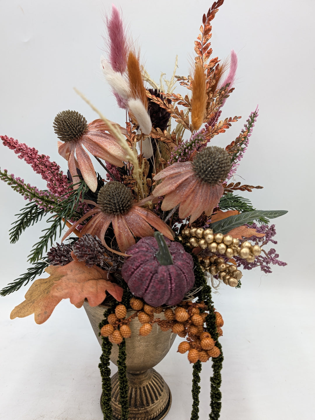 Nahaufnahme des Herbstgestecks: Sonnenhut, goldene Beeren, Eichenblatt und Kürbis über dem Rand der Vase