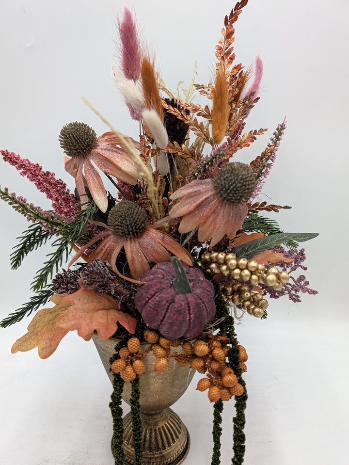 Nahaufnahme des Herbstgestecks: Sonnenhut, goldene Beeren, Eichenblatt und Kürbis über dem Rand der Vase