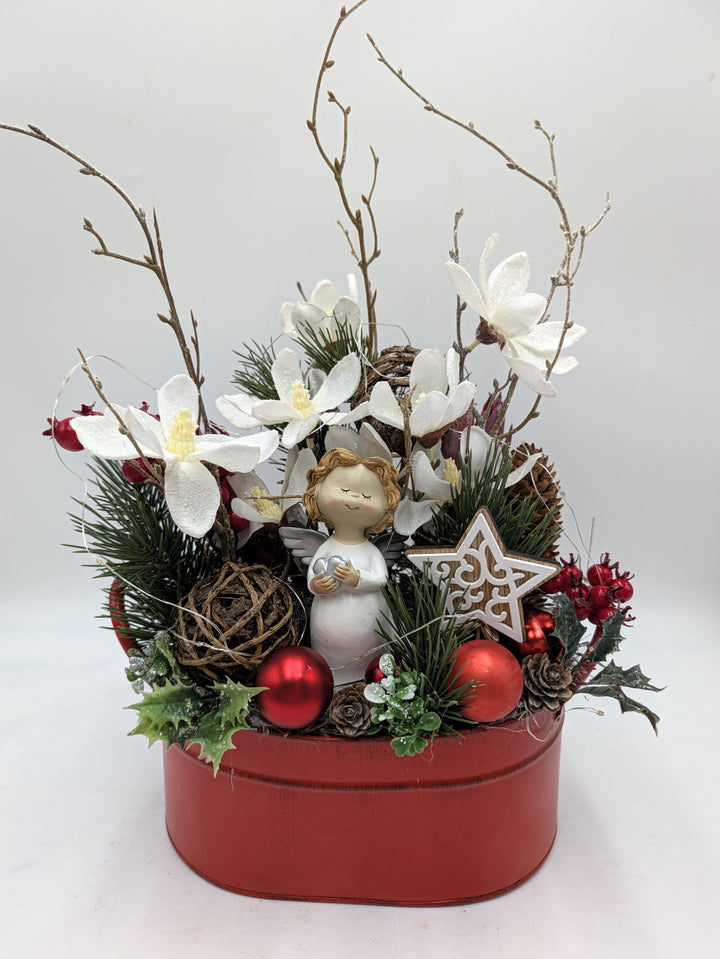 Weihnachtsgesteck mit Engelfigur, weißen Magnolien, roten Kugeln und Zweigen in roter Metallschale