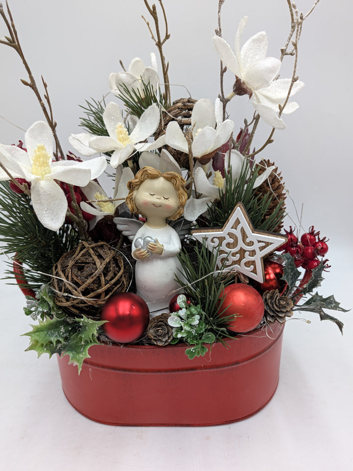 Nahsicht auf Engel mit Herz, Holzstern, Rebenkugel, Zapfen und roten Kugeln im weihnachtlichen Gesteck