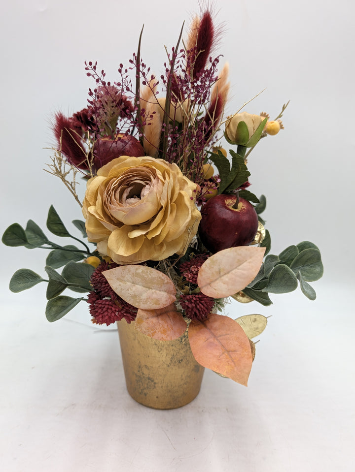 Herbstgesteck mit beiger Rose, dunkelrotem Apfel, Sedum und Gräsern in goldfarbenem Topf