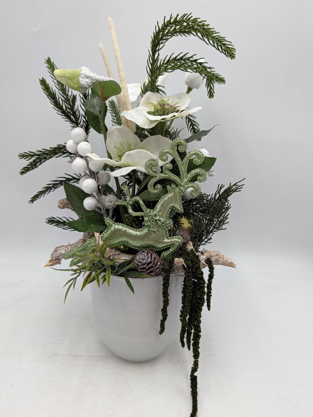 Wintergesteck im weißen Topf mit Christrosen, grünem Glitzerhirsch, weißen Beeren und hängendem Amarant