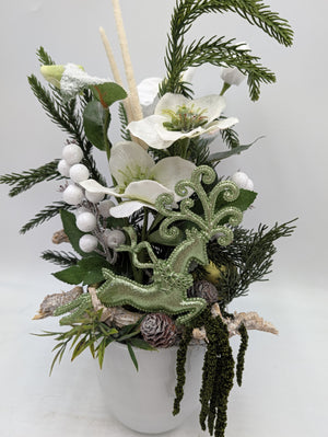 Nahaufnahme des Gestecks: weiße Christrosen, Tannenzweige, Zapfen, Rinde und grüner Hirsch mit Ornament