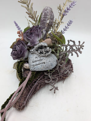 Trauergesteck mit grauem Herzstein, Engelfigur, lila Rosen und Lavendel auf Reisignest, seitlich fotografiert