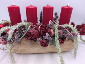 Nahaufnahme des Adventsgestecks mit dunkelroten Rosen, gefrosteten Beeren, Zapfen und roten Kugeln in heller Holzschale