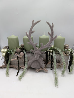 Adventsgesteck im Holzkasten mit vier mintgrünen Kerzen, grauem Hirsch, Zapfen und Kugeln, Kiefernzweige hängen seitlich