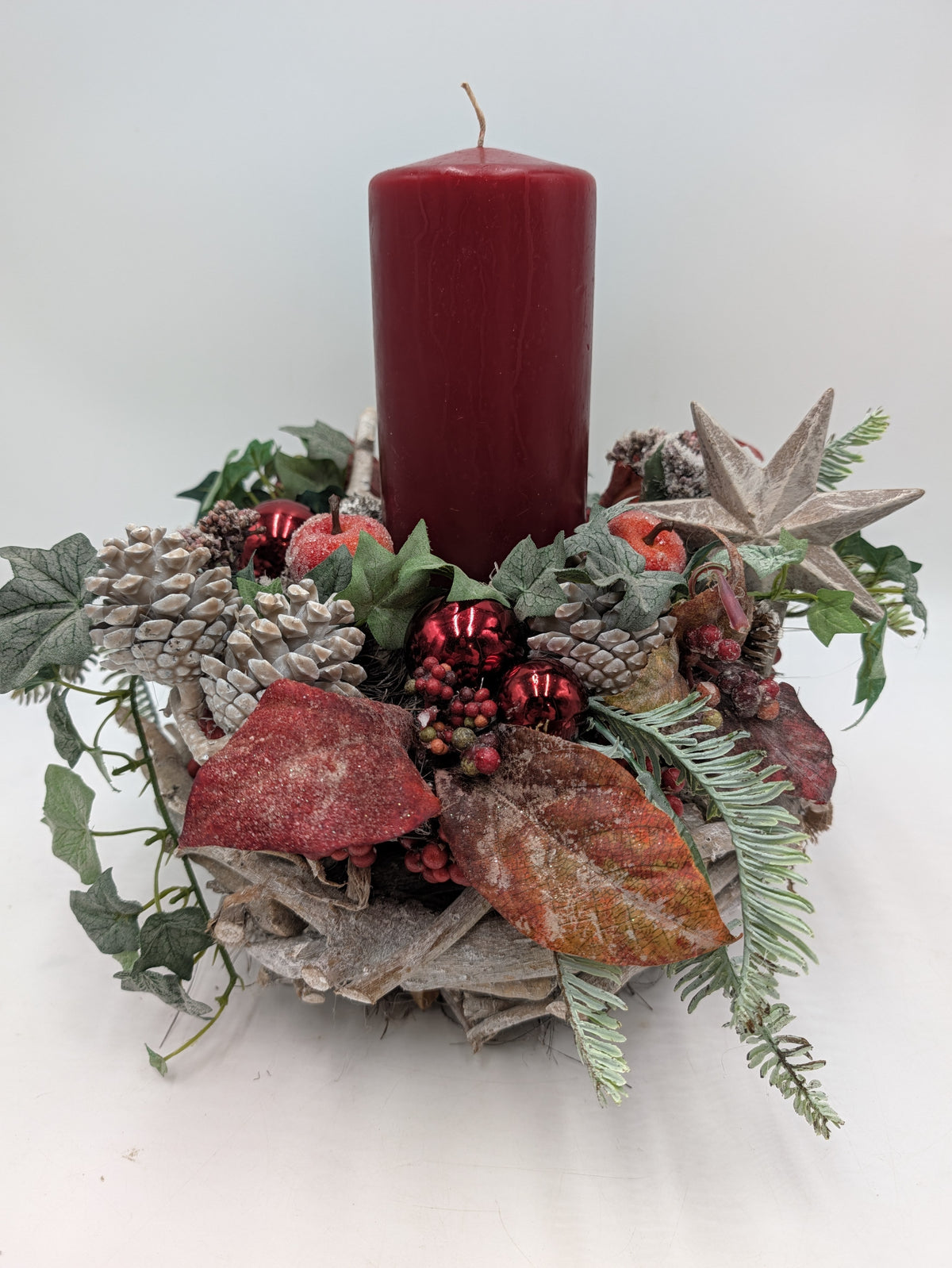 Adventsgesteck mit roter Stumpenkerze, weissen Zapfen, roten Kugeln und Holzstern auf Holzkranz