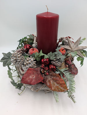 Adventsgesteck von der Seite: rote Kerze, Efeuranken, rote Äpfel, Beeren und gefrostete Tannenzweige