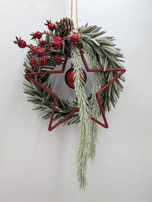 Weihnachtskranz an Juteschlaufe, roter Stern mit matter Kugel, Beerenzweige und herabhängender Tannenzweig