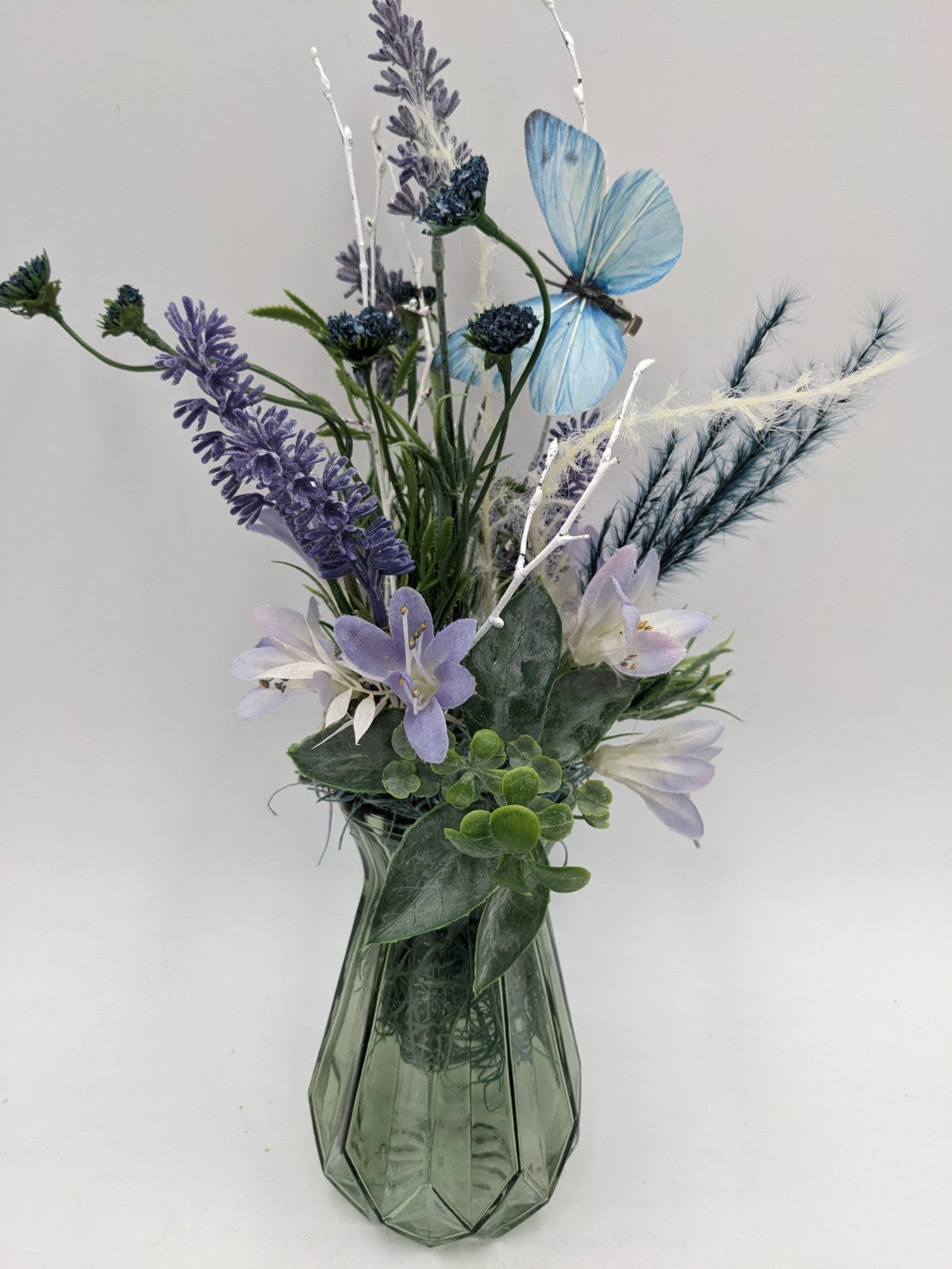 Schmales Sommergesteck mit lila Lavendel, blauem Schmetterling und Gräsern in grüner Glasvase, 37 cm hoch