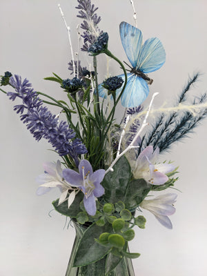 Nahaufnahme der Blüten: Lavendel, dunkelblaue Disteln, helllila Blüten, grüne Blätter und blauer Schmetterling