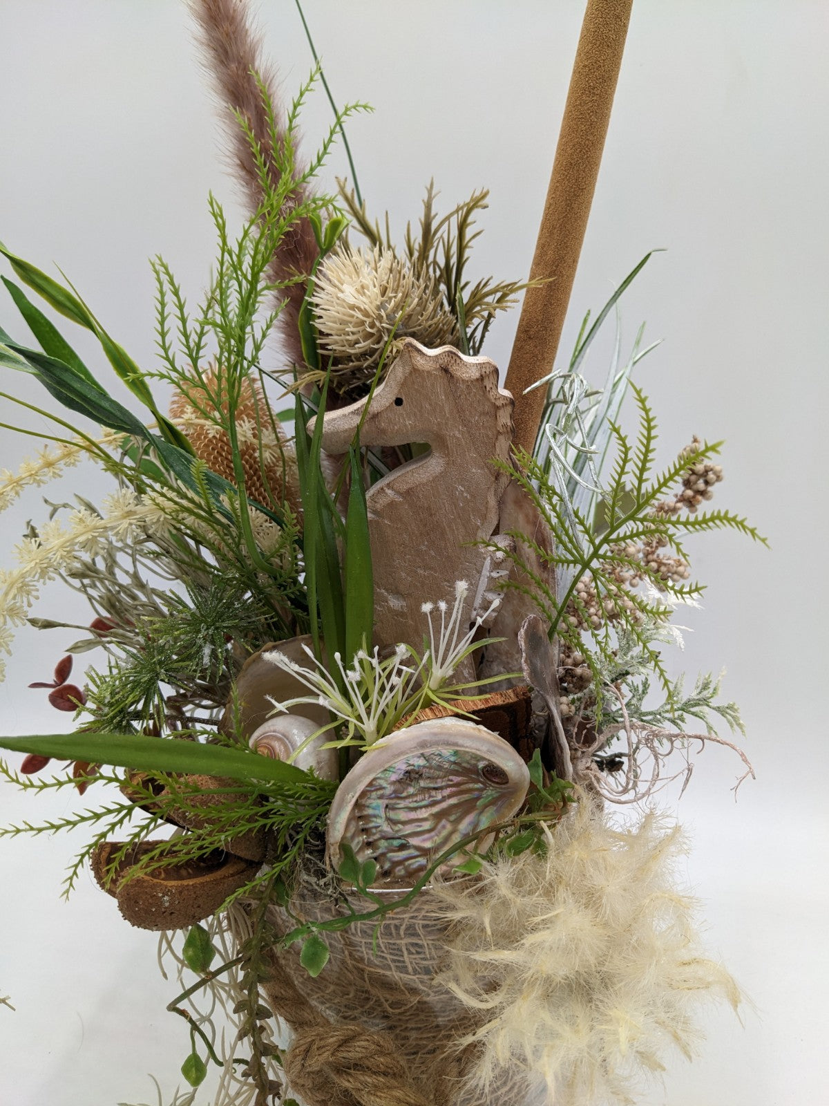 Detail des Gestecks: Holz-Seepferdchen, Perlmuttmuschel, cremefarbene Distel und grüne Farnwedel