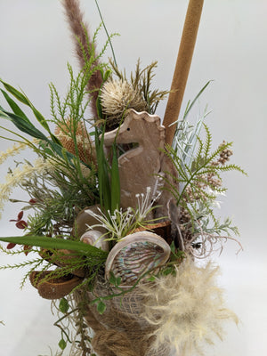 Detail des Gestecks: Holz-Seepferdchen, Perlmuttmuschel, cremefarbene Distel und grüne Farnwedel