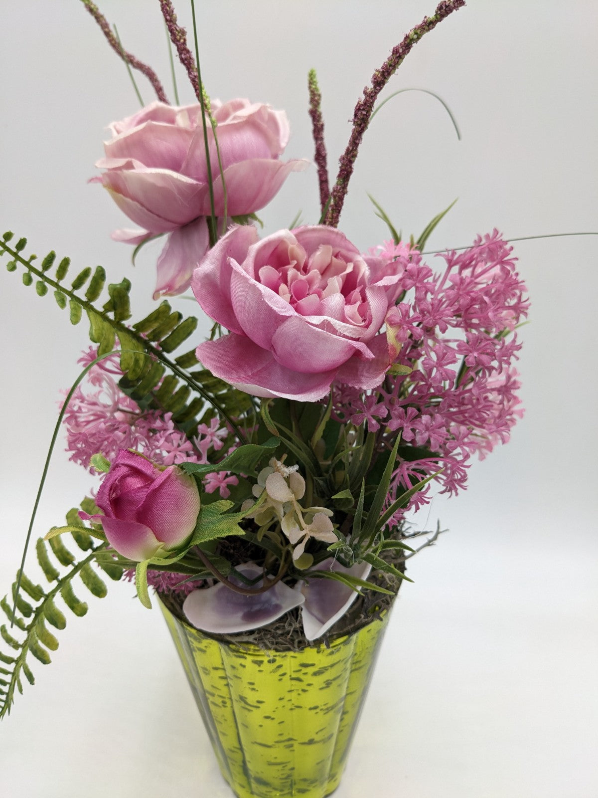 Nahaufnahme der rosa Rosen und Blütendolden über Muschelschalen und Moos am Topfrand
