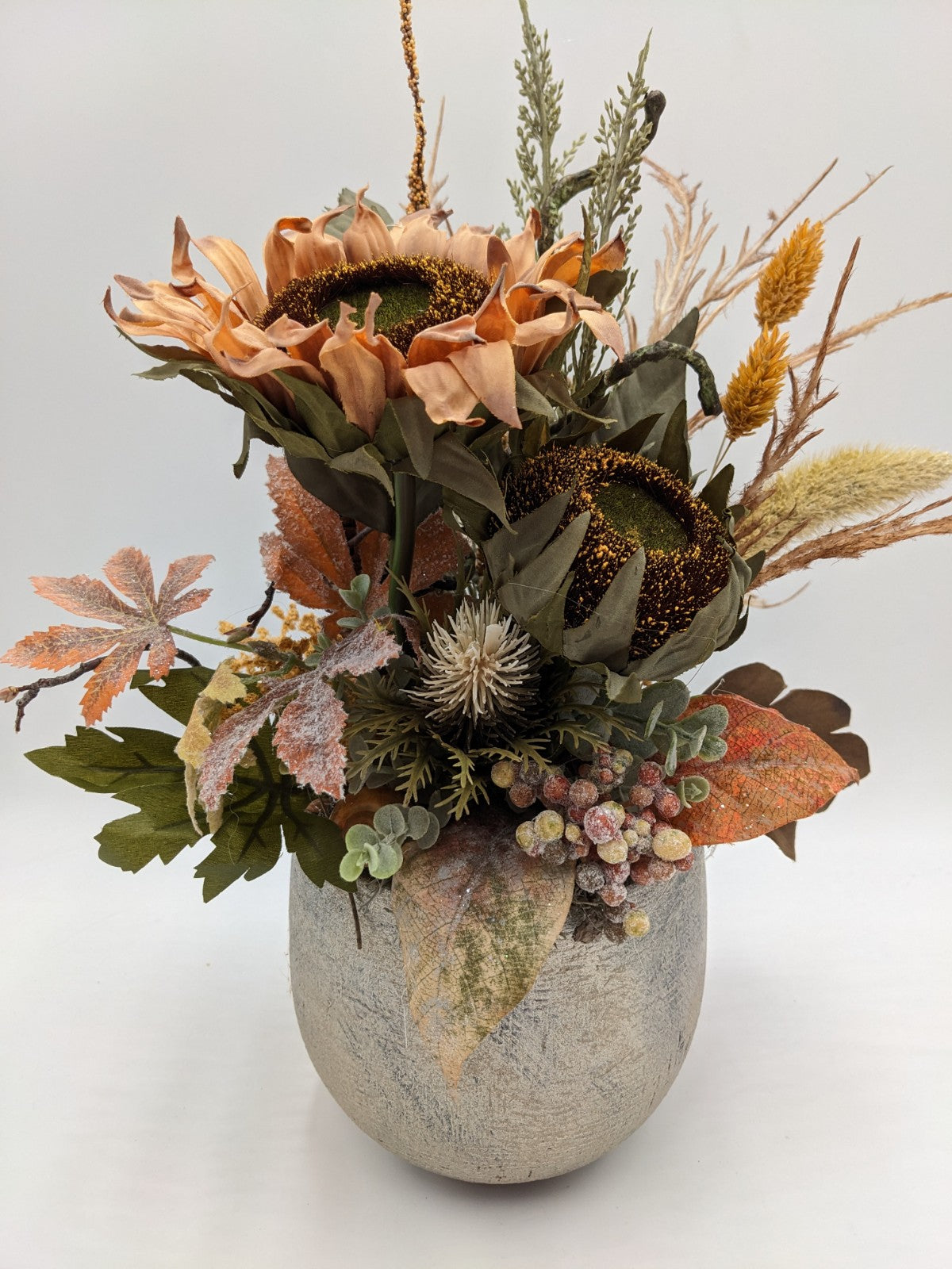 Gesteck mit zwei apricotfarbenen Sonnenblumen, Laub, Beeren und Gräsern in grauem Steintopf