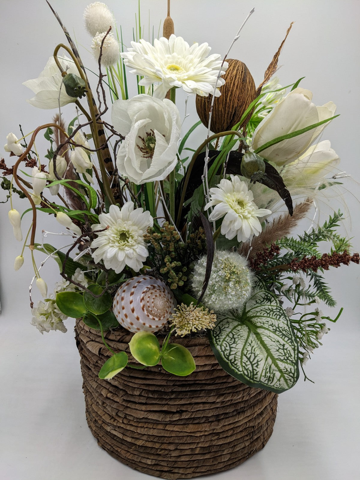 Sommergesteck im Korb mit weißen Gerbera, Tulpen, Gräsern, Kokosfrucht und Schneckenmuschel, 55 cm hoch
