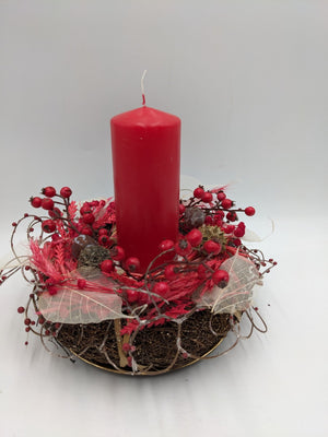 Herbstgesteck mit roter Stumpenkerze, roten Beeren, Gräsern und hellen Skelettblättern auf goldfarbenem Teller