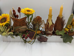 Langes Herbstgesteck im weißen Holztablett mit gelben Sonnenblumen, Holzeule, zwei gelben Kerzen und Maiskolben