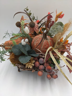 Herbstgesteck von der Seite: zwei Kürbisse, Eukalyptus, rotbraune Trauben, Zapfen und helle Ähren