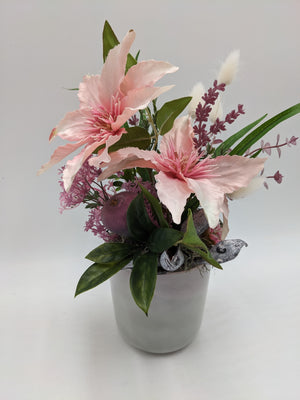 Tischgesteck in Rosa und Lila mit Clematis, Eukalyptus, Schoten und dunkler Frucht im grauen Topf