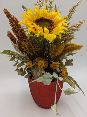 Herbstgesteck von vorn: Sonnenblume, senfgelbe Schafgarbe, braune Rispen und Efeuranke über rotem Topf