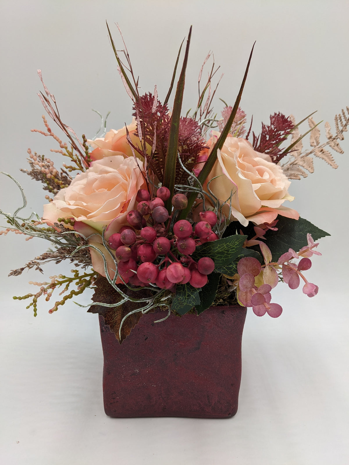Herbstgesteck mit apricotfarbenen Rosen, roten Beeren und Gräsern in weinrotem quadratischem Topf