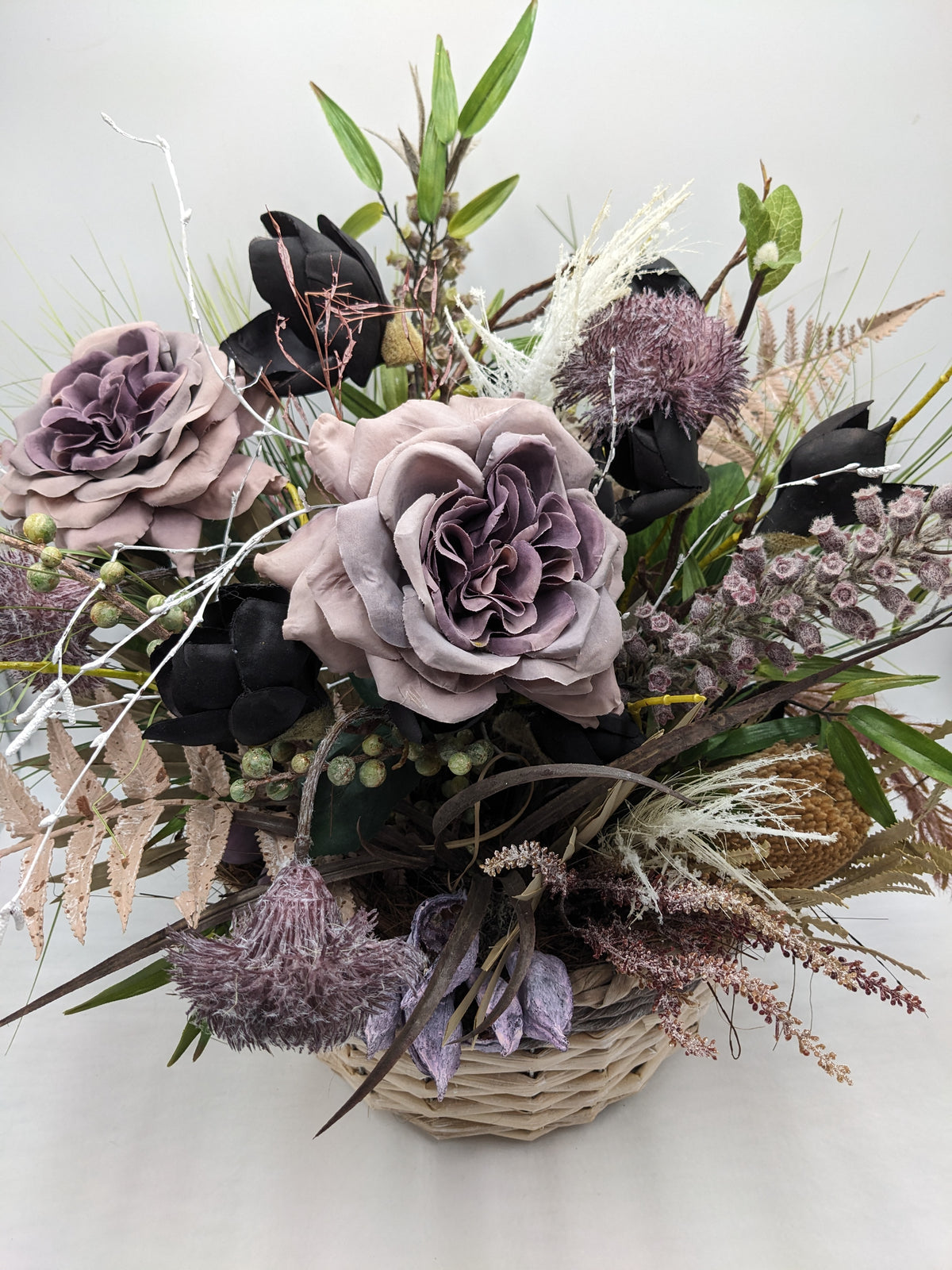 Nahaufnahme der lilafarbenen Rosen, schwarzen Magnolienknospen und hellen Gräser im Korbgesteck