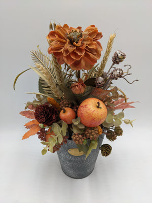 Herbstgesteck von oben: orange Blüte, zwei Äpfel, dunkelrote Blüte, Eukalyptus und Weizen im Zinktopf