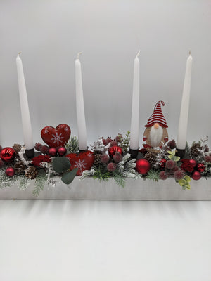 Langes Adventsgesteck mit vier weißen Stabkerzen, roten Kugeln, Herzen und Wichtel in weißem Holztablett