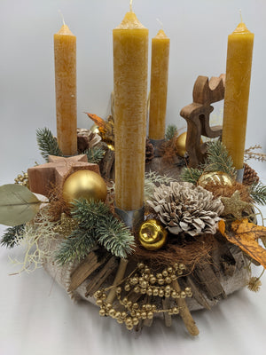 Adventskranz aus Treibholz mit vier senfgelben Stabkerzen, goldenen Kugeln, Zapfen und Holzhirsch, schräg von vorn