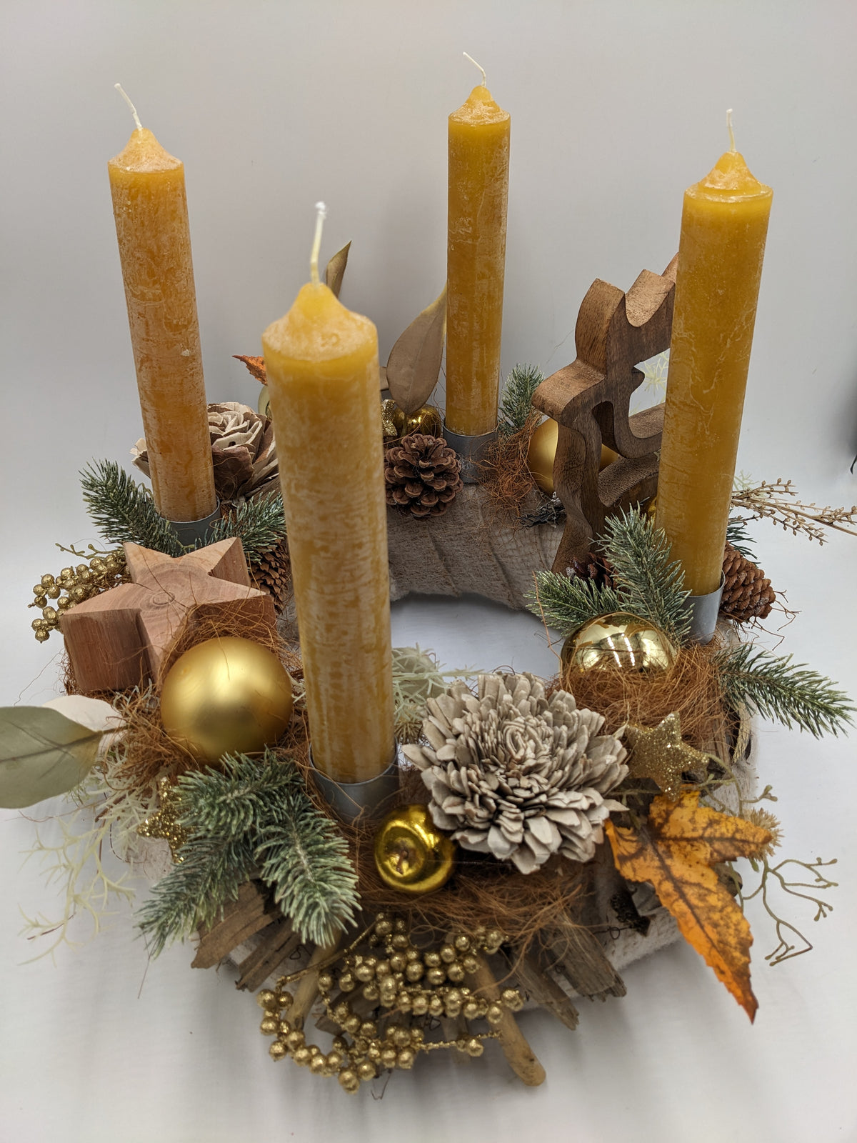 Adventskranz von oben: runder Holzkranz mit vier senfgelben Kerzen, goldenem Apfel, Holzsternen und Tannenzweigen
