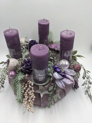 Adventskranz von schräg oben: lila Filzrund mit vier Kerzen, Herz, Beerenzweigen, Schoten und Tannenzweigen