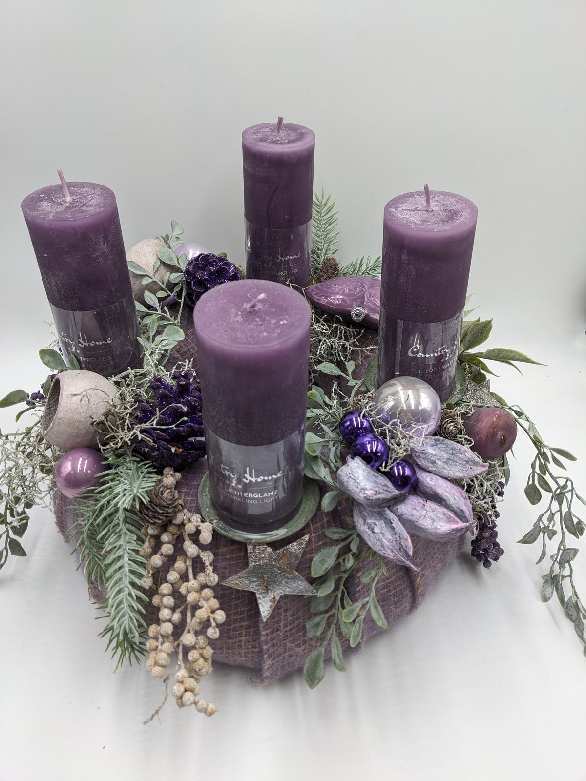 Adventskranz von schräg oben: lila Filzrund mit vier Kerzen, Herz, Beerenzweigen, Schoten und Tannenzweigen